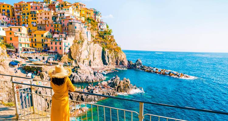 Bâtiments colorés à flanc de falaise dans les Cinque Terre avec une femme contemplant la mer.