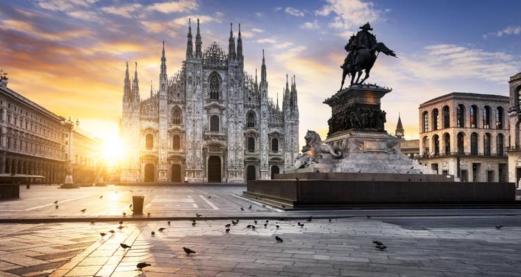 Vue de la cathédrale de Milan avec une statue au premier plan pendant le coucher du soleil.