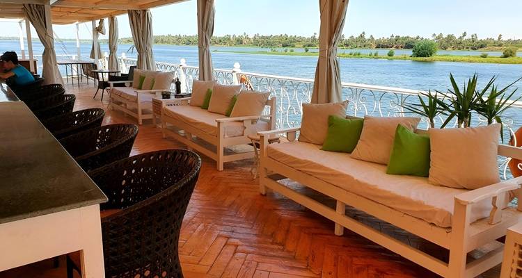 Ship's deck with seating overlooking a river.