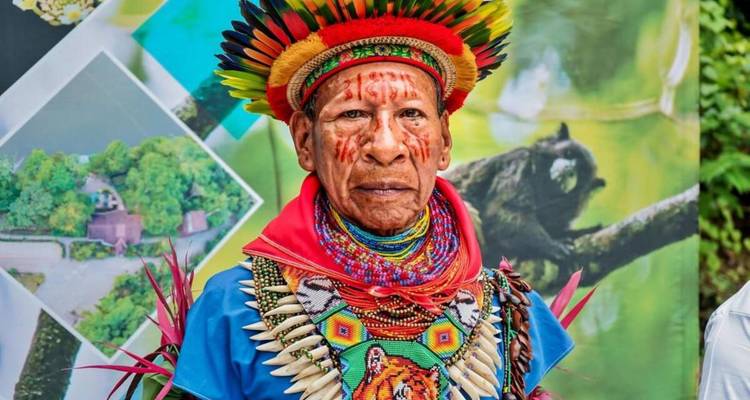 Indigenous man in traditional attire with a rainforest background.