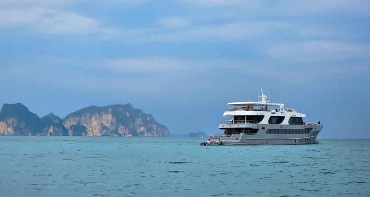 Yacht d'expédition ancré dans des eaux turquoise avec des îles rocheuses lointaines sous un ciel bleu.