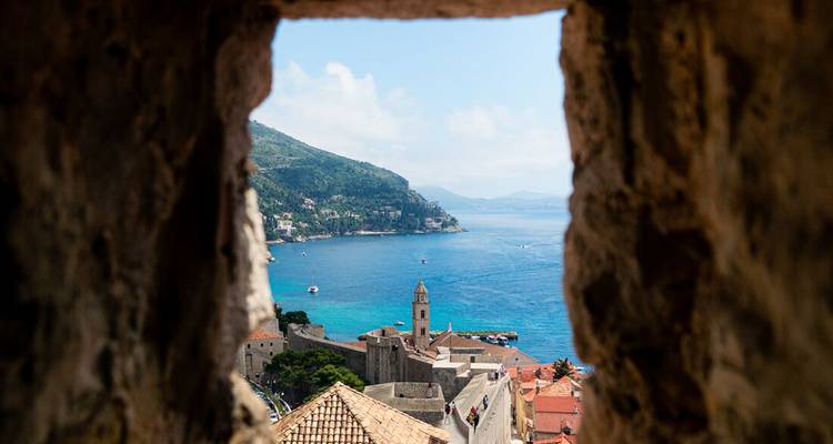 Vue d'une ville côtière à travers une ouverture dans un vieux mur.