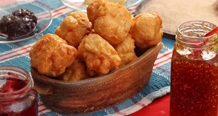 Panier de pâtisseries frites et pots de confiture sur une nappe.