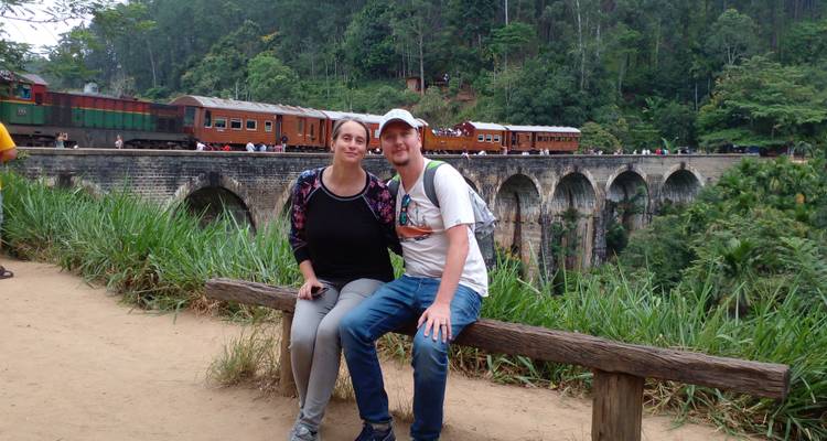 Couple assis sur un banc avec un train pittoresque et un pont en arrière-plan.