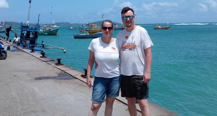 Couple posant près de la mer avec des bateaux colorés en arrière-plan.