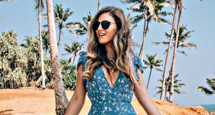 Une femme en robe bleue se tenant parmi des palmiers sous un ciel dégagé.