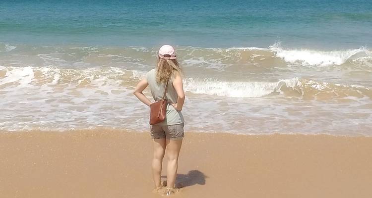 Woman standing on a sandy beach looking at the ocean.