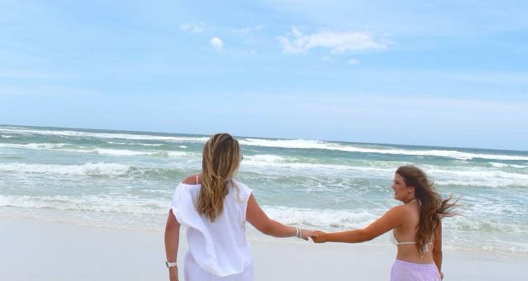 Two women holding hands on a sunny beach.