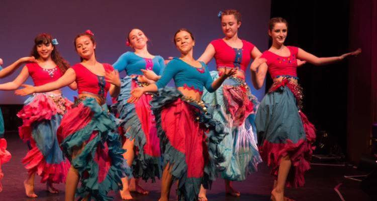 Grupo de bailarines actuando en el escenario con trajes vibrantes.