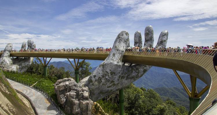 Golden Bridge held by large hands over lush mountains.