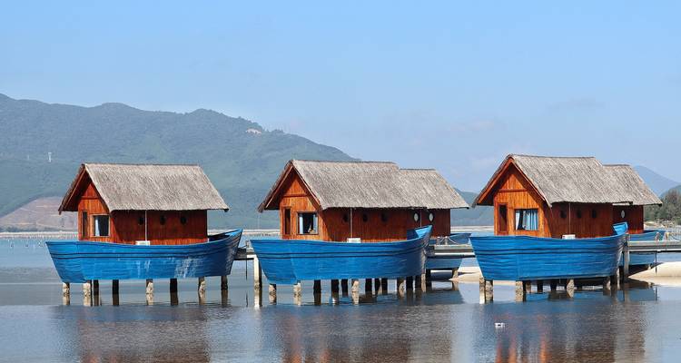 Three houseboats on stilts along a calm body of water.