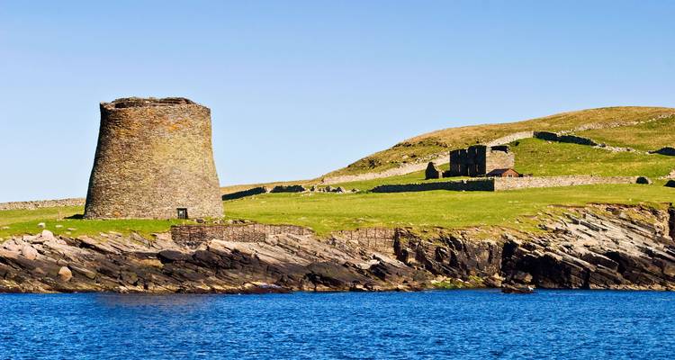 Ruines anciennes sur un littoral sous un ciel bleu clair.