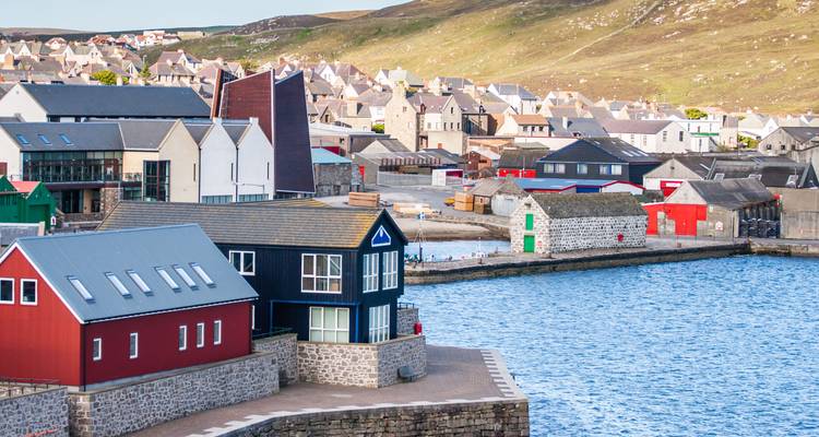 Bâtiments colorés près d'un port avec des collines en arrière-plan.