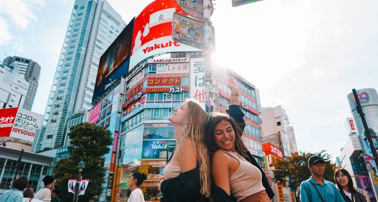 Zwei Frauen posieren für ein Foto auf einem belebten Stadtplatz.