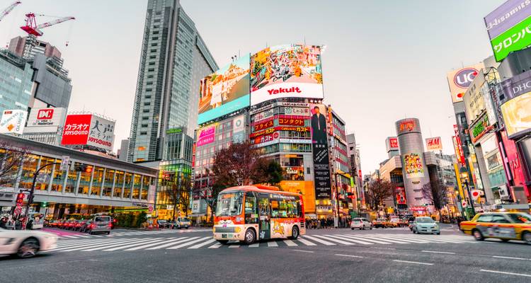Belebte Stadtkreuzung mit Menschen, Fahrzeugen und hohen Gebäuden.