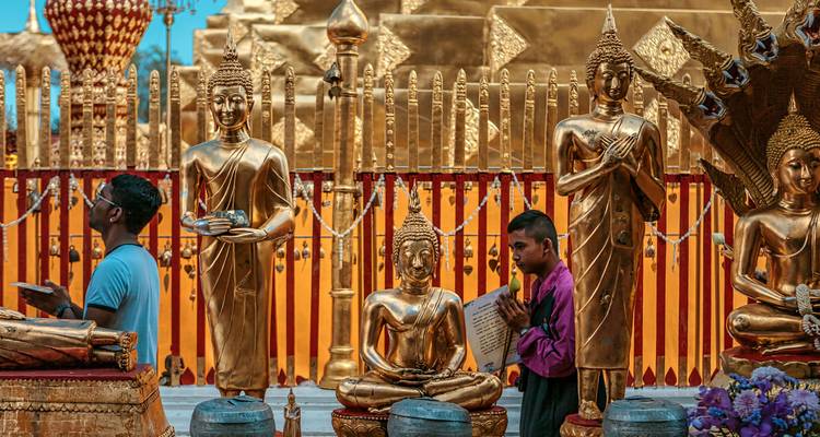 Des gens priant parmi des statues bouddhistes dorées dans un temple.