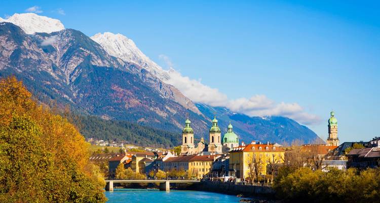 Eine Stadt mit Barockarchitektur und einem Fluss vor Bergkulisse.