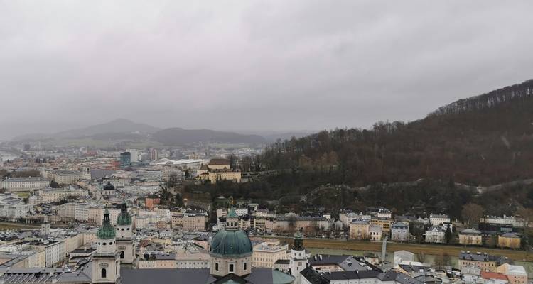 Bewölkte Stadtlandschaft mit historischen Gebäuden und Hügeln.
