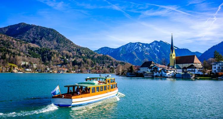 Boot, das auf einem See fährt, mit Bergen und einer Kirche im Hintergrund.