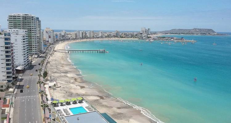 Ciudad costera panorámica con una playa de arena blanca curva y agua turquesa respaldada por torres de gran altura.