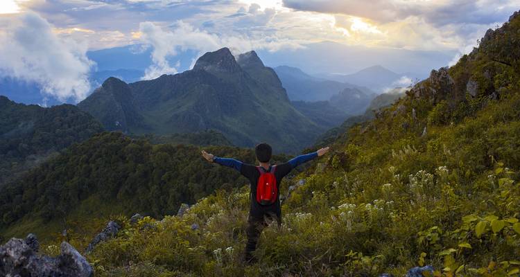 A hiker with arms outstretched overlooking a mountainous landscape.