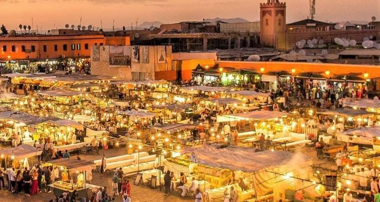 Geschäftiger marokkanischer Marktplatz bei Sonnenuntergang mit hellen Lichtern und emsigen Händlern.
