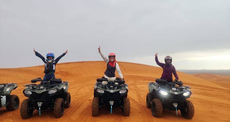 Trois personnes faisant du quad dans un désert, faisant des signes de victoire.