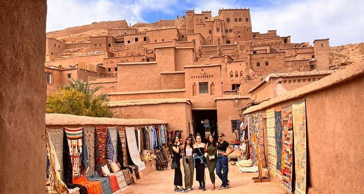Un groupe de personnes marchant dans une rue bordée de textiles colorés et de bâtiments traditionnels.