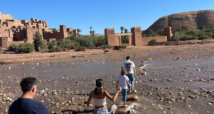 Des personnes traversant une rivière peu profonde pour atteindre une structure historique.