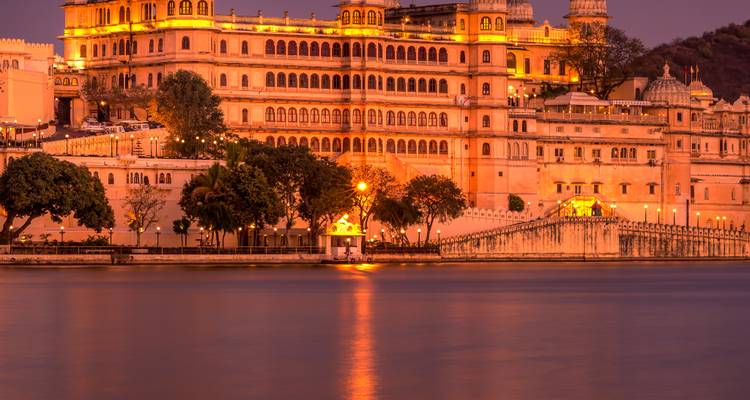 Palais de la ville illuminé à Udaipur au bord de l'eau au crépuscule.
