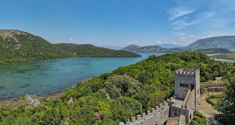 Un vieux fort au bord d'un lac serein avec des montagnes à l'arrière-plan.
