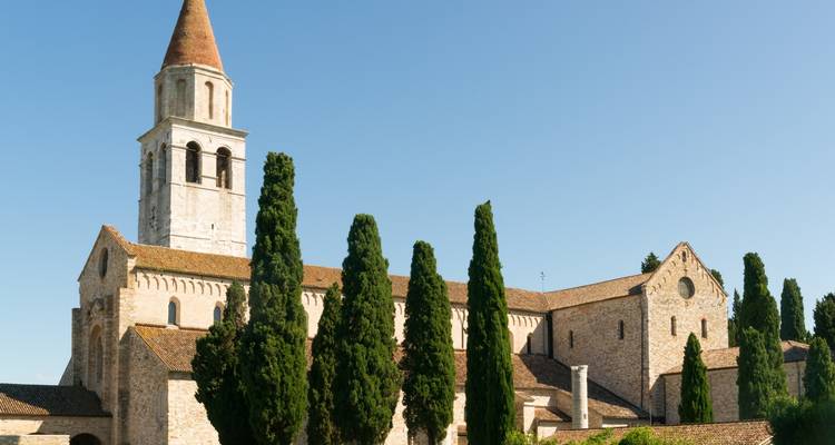 Église historique avec un haut clocher entourée d'arbres.