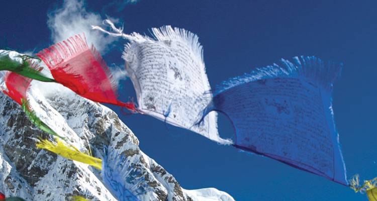 Des drapeaux de prière colorés flottant devant un décor de montagnes enneigées.