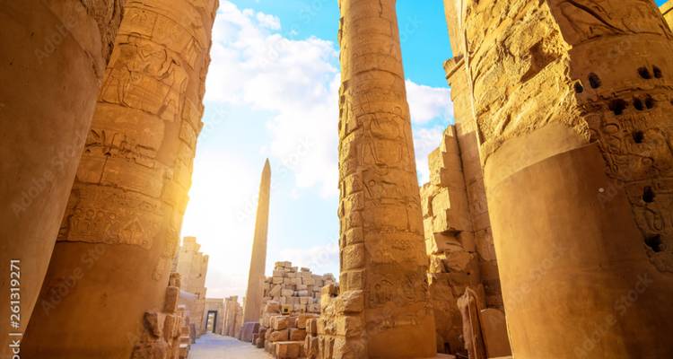 Zonovergoten zaal met torenhoge zandstenen zuilen en een obelisk in een oud-Egyptische tempel.