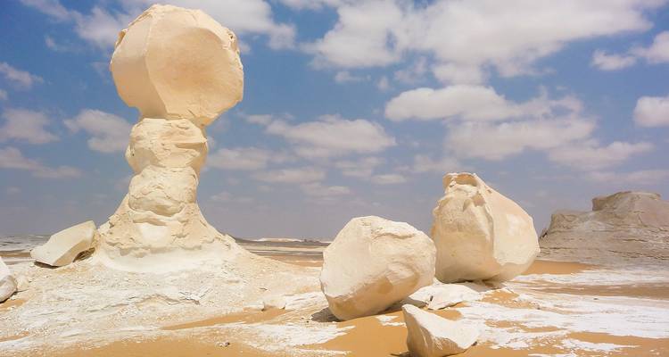 Surrealistische krijtwitte rotsformaties rijzen op uit het gouden zand van Egypte's Witte Woestijn onder gevlekte wolken.