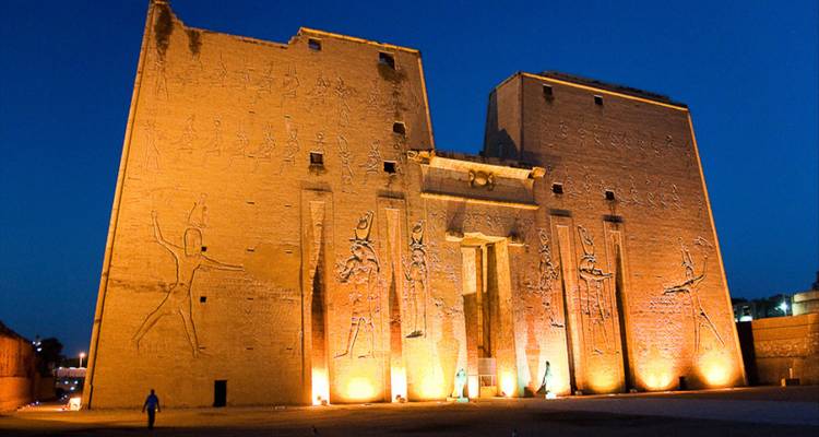 Massieve verlichte zandstenen pyloon bedekt met hiërogliefen bij een oude Egyptische tempel tegen een diepblauwe schemering