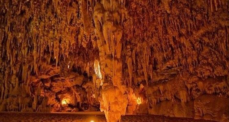 Interior de cueva de piedra caliza iluminada llena de dramáticas estalactitas y estalagmitas iluminadas por lámparas cálidas.