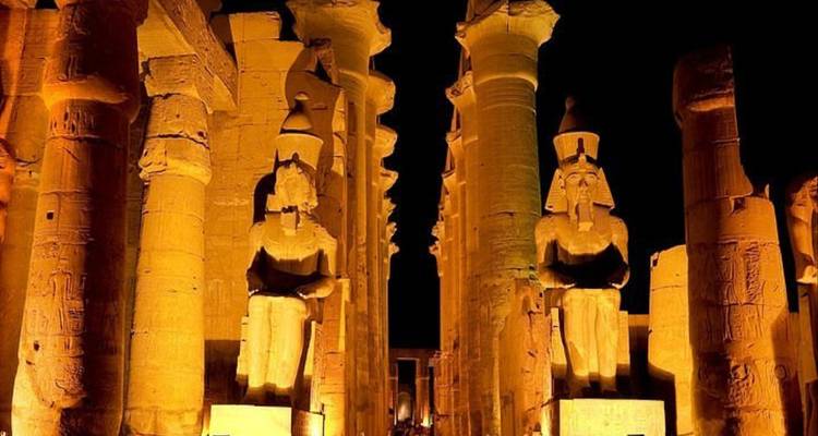 Estatuas iluminadas de faraones sentados flanqueadas por columnas imponentes dentro del Templo de Luxor por la noche.