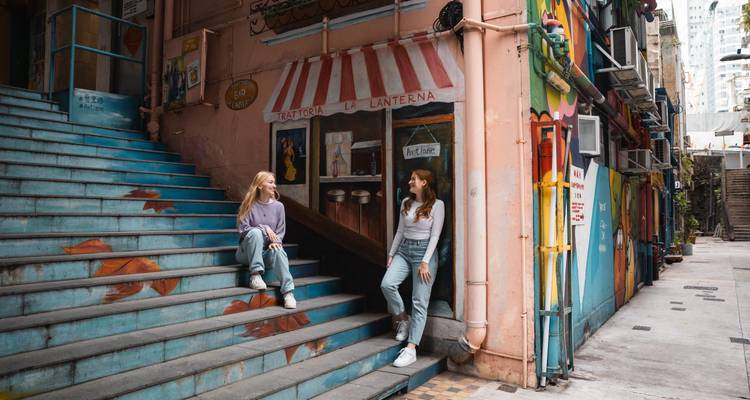 Two women sitting on colorful stairs near a painted wall in an urban setting.