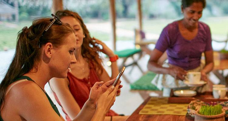 Menschen sitzen an einem Tisch in einer rustikalen Umgebung, wobei einer ein Telefon benutzt.