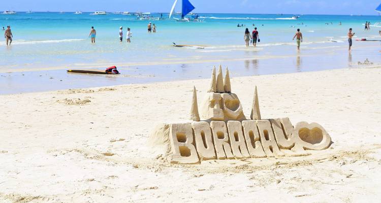Plage de sable avec des gens et un château de sable épelant Boracay.