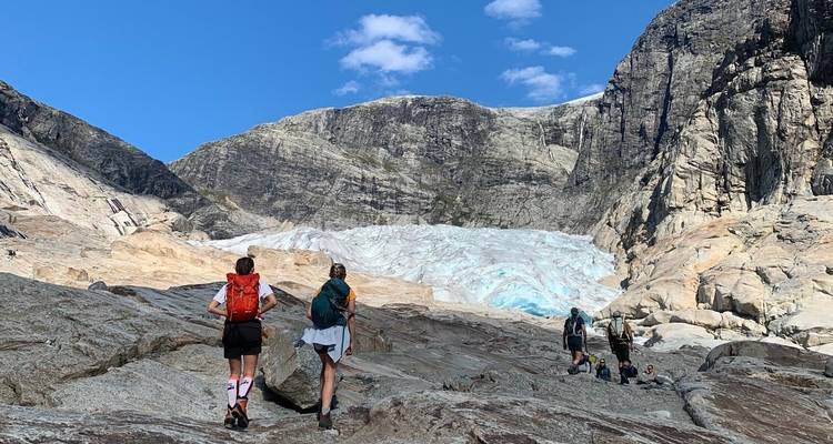 Los excursionistas se acercan a una lengua glacial azul enmarcada por paredes rocosas escarpadas bajo un cielo brillante.