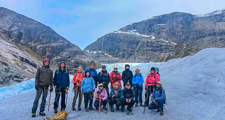 Un gran grupo de senderismo posa junto en un glaciar helado rodeado de montañas empinadas.