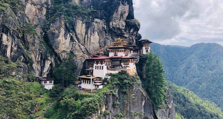 Monastère de Taktsang sur une falaise escarpée entouré d'une forêt luxuriante.
