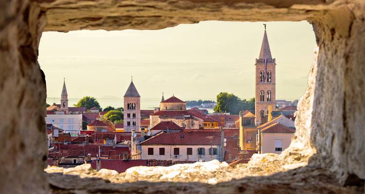 Vue à travers une fenêtre en pierre révélant un paysage urbain avec des tours.