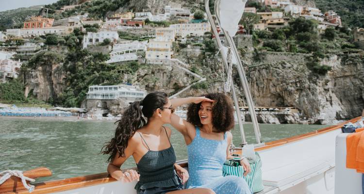 Deux femmes assises sur un bateau avec des maisons colorées à flanc de colline en arrière-plan.