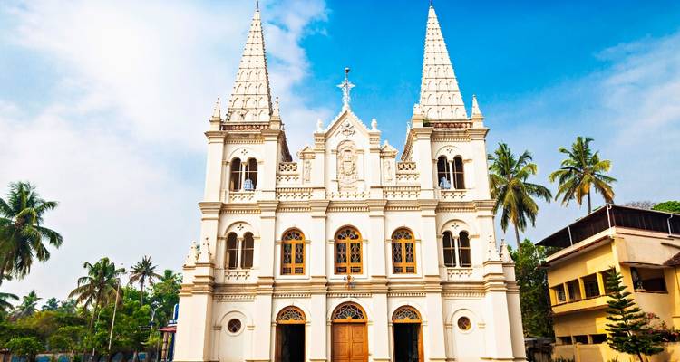 Une basilique de l'époque coloniale d'un blanc éclatant, aux deux clochers jumeaux, s'élève sous un ciel bleu vif bordé de palmiers.