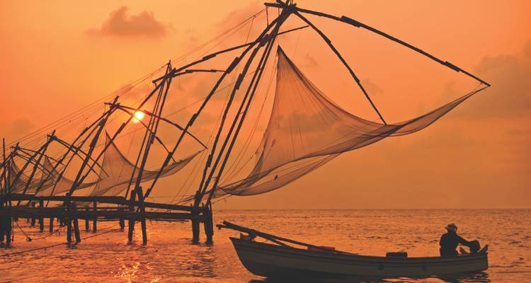 Les filets de pêche chinois se dessinent en silhouette au-dessus d'une eau teintée d'orange au coucher du soleil, avec un bateau solitaire en dessous.