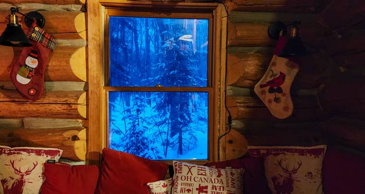 Intérieur de chalet douillet avec décorations de Noël et vue enneigée par la fenêtre.