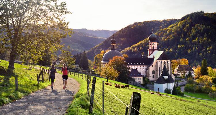 Deux randonneurs marchant dans un paysage pastoral vers un site historique.